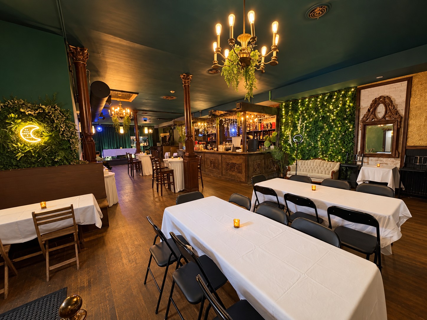 Chandeliers over dining tables beside the Moonlight Lounge greenery wall and sofa